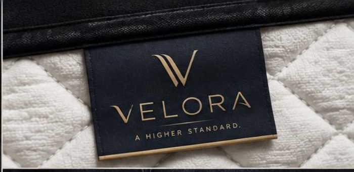 Close-up of the navy and gold VELORA label stitched onto a quilted mattress cover